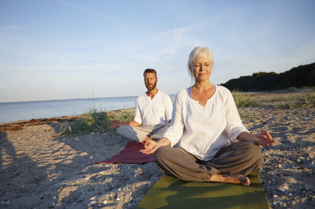 Äldre par praktiserar Yoga på stranden nära vattnet - Ayurveda och Yoga för viktminskning