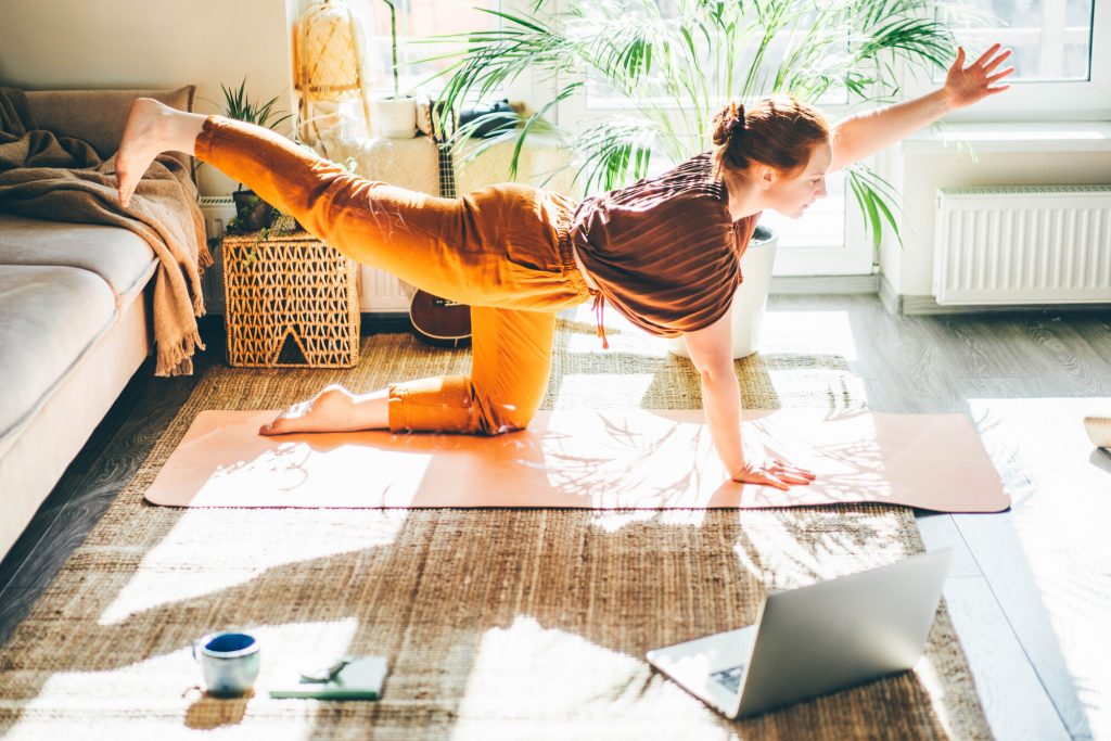 Ung kvinna praktiserar yoga i sitt vardagsrum hemma.