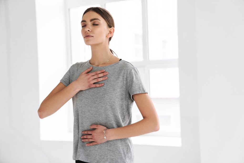 Ung kvinna övar på andningen med en hand på bröstet och en hand på magen.