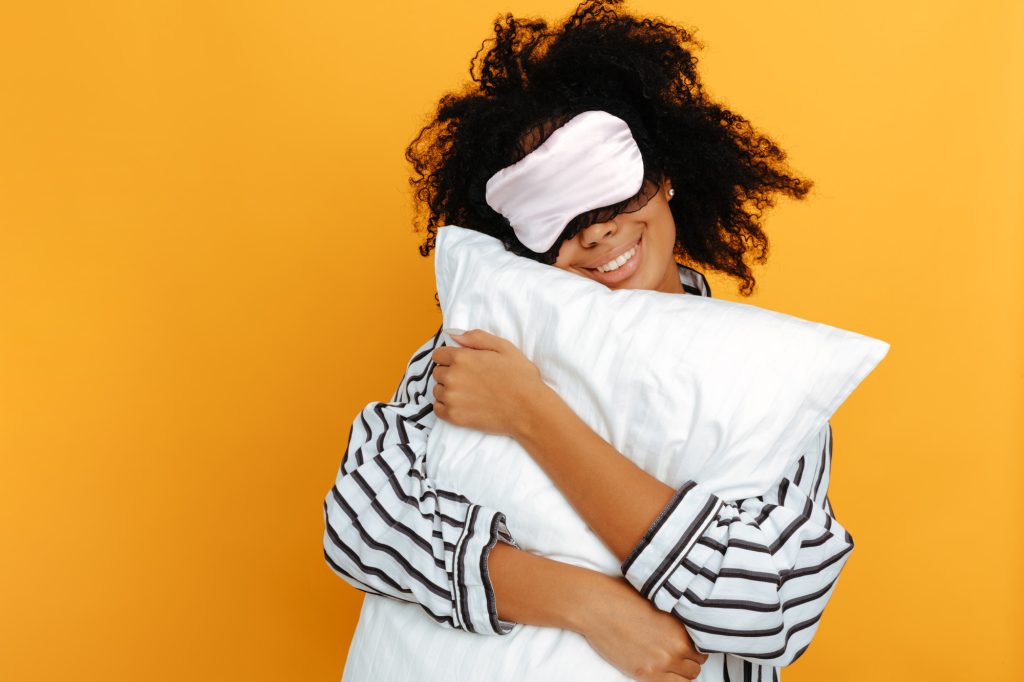 Ung kvinna i pyjamas, med sovmask och kudde.