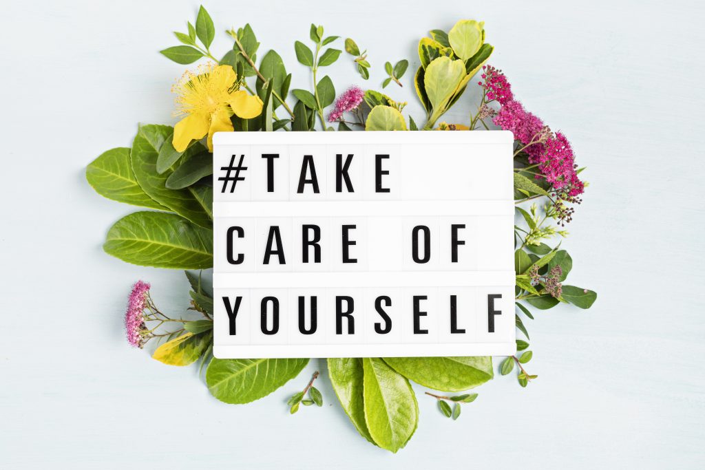 Löv och blomstrar bakom en skylt med texten #Take care of yourself